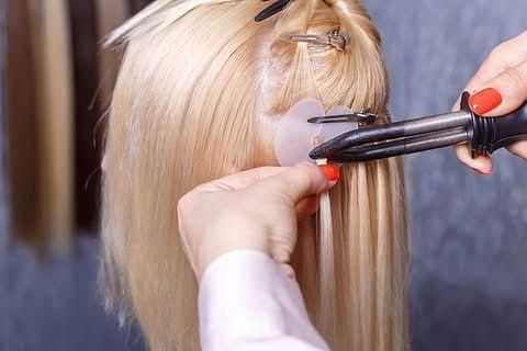 Hair stylist curling blonde extensions with an iron.